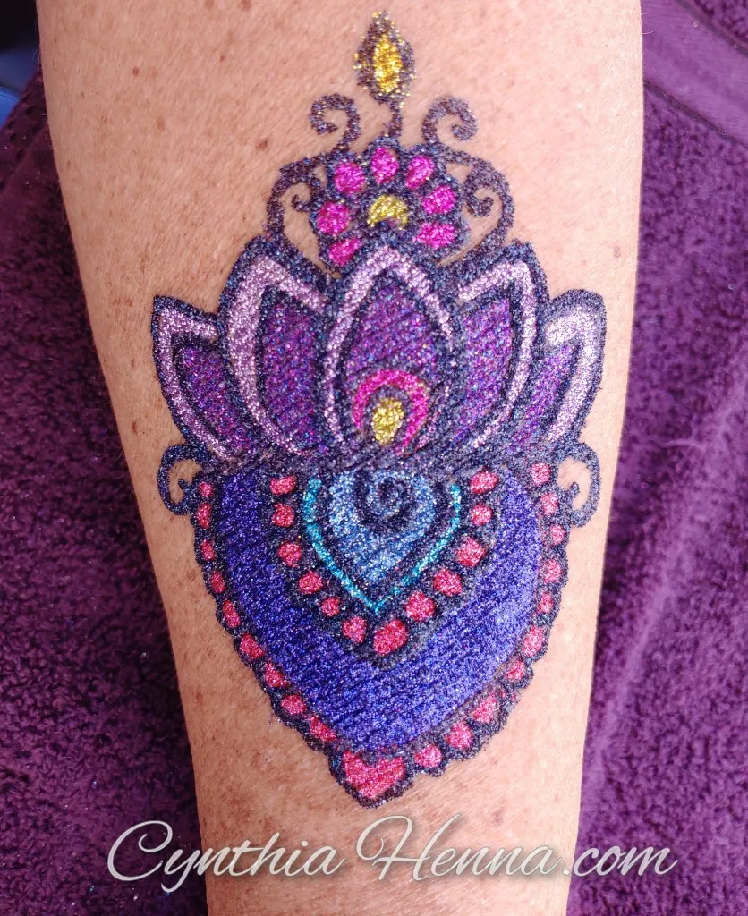 Large freehand glitter tattoo of a purple and pink lotus on a guest's leg
