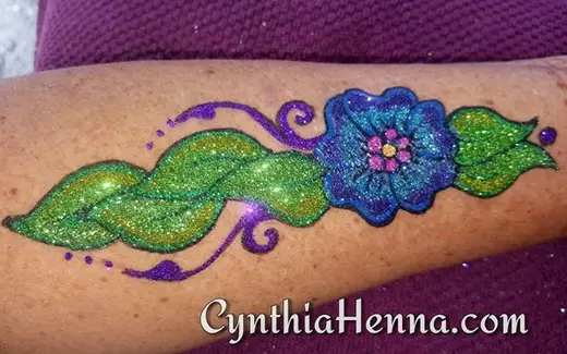 Freehand glitter flower and leaves in green, blue and purple on a forearm