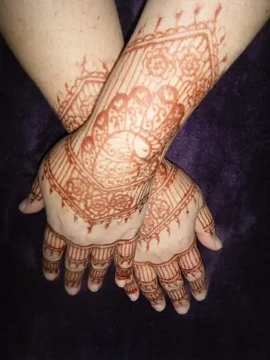Matching henna cuffs and finger work on two hands resting on purple velvet