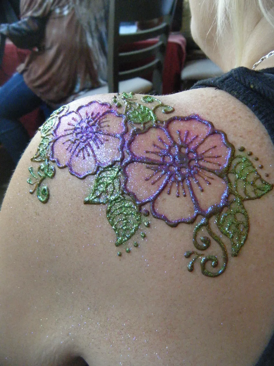 Fresh henna hibiscus design on a guest's shoulder, outlined with green and purple cosmetic glitter